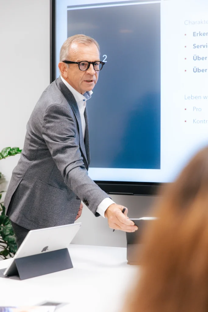 Blick über die Schulter zu einer Person vor einem digitalen Whiteboard, er hält eine Präsentation